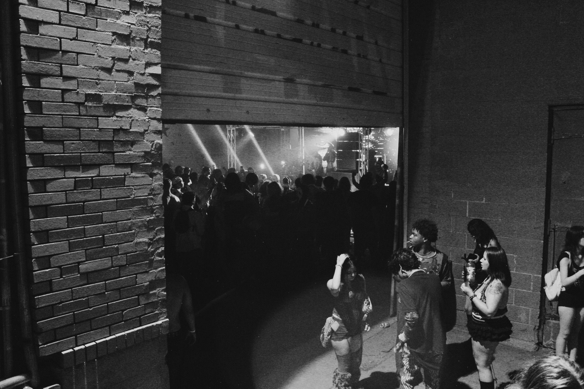 An open warehouse doorway looking into a crowd and illuminated stage in black and white.